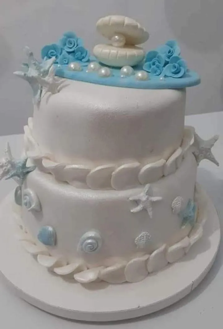 Bolo de dois andares branco decorado com conchas, estrelas do mar e flores azuis em fondant